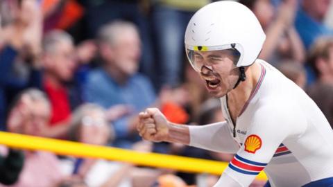 Charlie Tanfield cheers his success on the bike. He is wearing a white jersey and a white helmet.