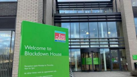 East Devon District Council headquarters showing a green sign and a brick building with large windows