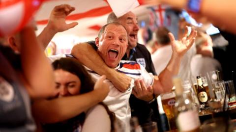 England fans cheers, raising the arms in the air, with pints in front of them