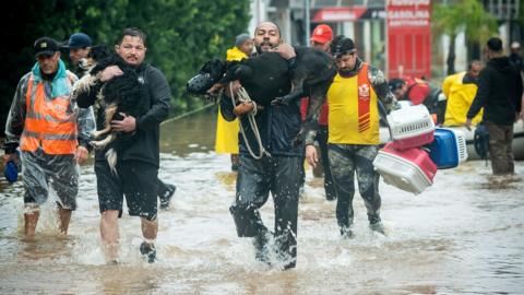 People carry dogs and belongings through floodwater in Porto Alegre in May 2024.