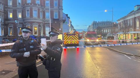 A picture of police officers standing in front of a cordon protecting the scene near to Exeter Central train station.