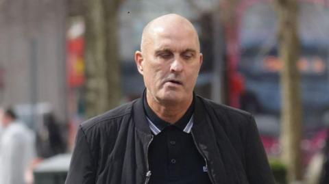 Derek George Lammey, a man wearing a black jacket, with black polo shirt. 