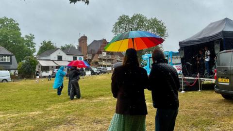 People shelter from the rain at an event using rain coats and colourful umbrellas