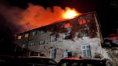 A picture of the roof of the building on fire. There is an orange glow and flame coming from the roof.