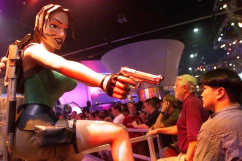 A giant sized model of Lara Croft aims a gun at a gaming convention crowd member 