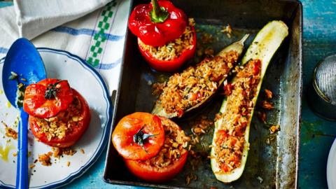 A baking tray holds two halves of stuffed courgette, a stuffed tomato and stuffed red pepper.