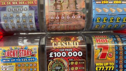 A close up picture of six scratchcard dispensers, coloured red, blue, and yellow. The bottom three dispensers read 'Lucky Stars', 'Casino' and 'Red Hot 7's'. 