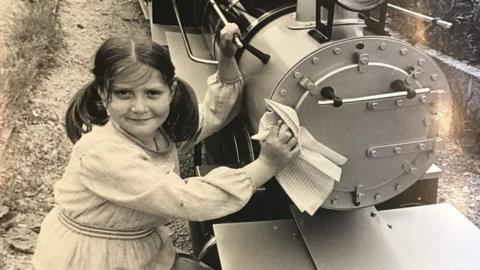 Emma Cole as a little girl in a black and white photo which shows her next to the miniature train.