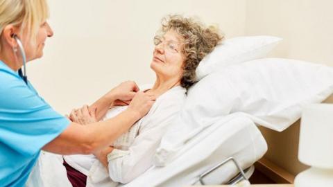 Woman in hospital bed with nurse dressed in blue offering support