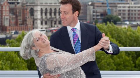 Ann Widdecombe dances with Anton du Beke in a ballroom pose with London skyline in background