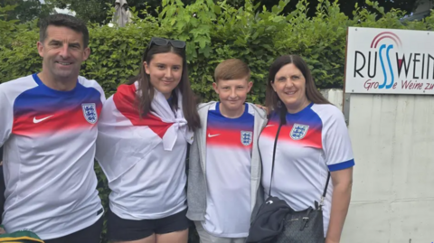 Kevin, Amelia, Ethan and Kelly are standing in a line wearing football tops.
