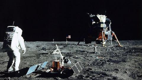 Astronaut Edwin E. Aldrin Jr. stands near a scientific experiment on the lunar surface wearing a space suit.