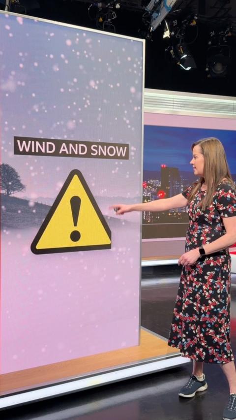Alexis Green stands in the studio pointing at a warning sign.