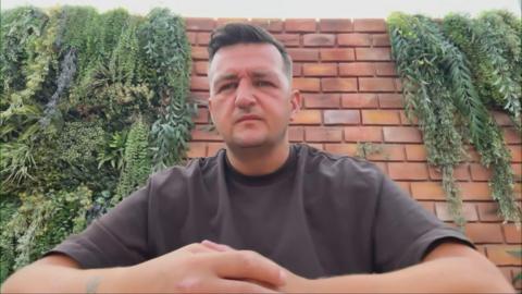 Gary Goldie looking right at the camera. He is wearing a brown T-shirt and is sitting in front of a brick wall.