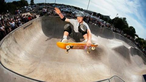 Tay Cunningham competing in the park, or 'bowl', event at the British National Championships last year, which he won. He is jumping out of the bowl, grabbing his board, with crowds lining the ridge of the ramp in the background