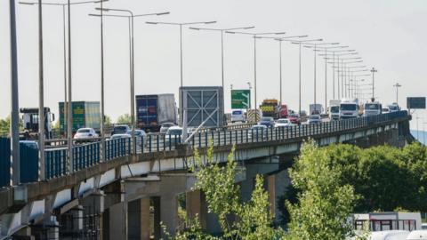 Tees flyover - both carriageways are visible and have a lot of vehicles driving over them. There are some green treetops visible at the bottom right, and the sky is a dull grey