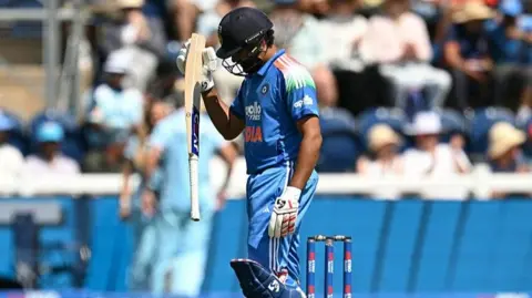 Rohit Sharma, wearing a blue India kit and dark blue helmet, walks off with his head down and his bat in his left hand
