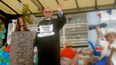 BBC CWR presenter Vic Minett stands on a float dressed as a vicar next to a woman dressed as a Bourbon biscuit and a woman sat down waving.