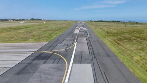 Alderney's Airport runway - Tarmac with patchwork all over it and grass either side.