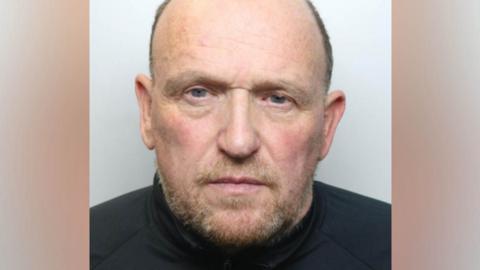 Martin has a brown greying beard, and cropped brown greyign hair and is wearing a black shirt.