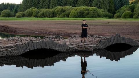 Stone bridge at the Llwyn-Onn Reservoir in Merthyr Tydfil in 2026. The bridge is visible above the water. A boy is standing on it