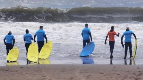 Six men with surfboards going into the North Sea and North Bay in Scarborough