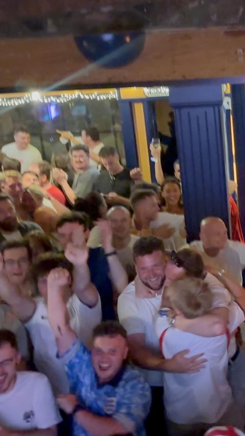 Multiple people hugging and celebrating in a pub