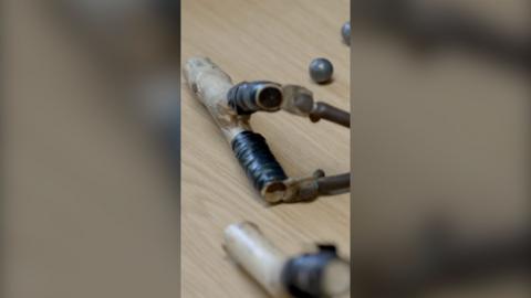 A close up of a hand-held wooden catapult with some ball bearings in the background.