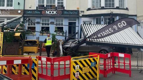 A car sitting among wreckage in front of the Nook bar, with temporary barriers in the foreground  