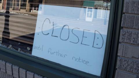 A handwritten sign placed in a shop window reads 'Closed until further notice'