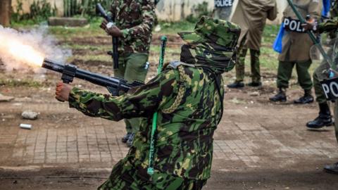 A masked Kenyan police officer fires a tear gas canister during a demonstration against tax hikes as Members of the Parliament vote the Finance Bill 2024 in downtown Nairobi, Kenya - 20 June 2024