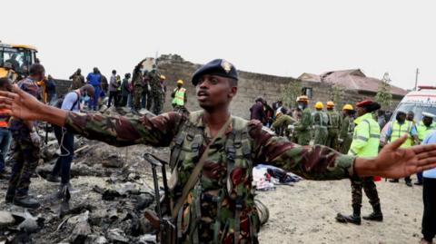 A member of the security forces holds his hands up as emergency workers work at the scene of a light aircraft crash in Nairobi, Kenya.