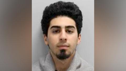 Police custody image of Marwan Khadir, a young man with curly black hair and a goatee beard.