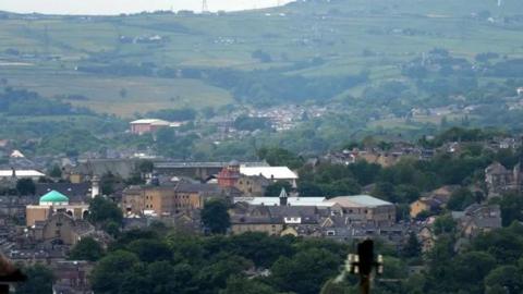 A view of the Bradford skyline, featuring tall buildings, trees and hills.