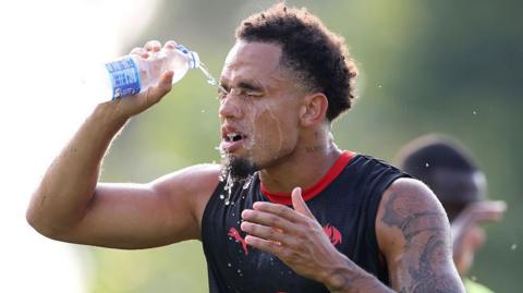 Noah Okafor pours water over his face to cool down during an AC Milan training session
