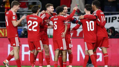 Wales players in red shirts celebrate a goal
