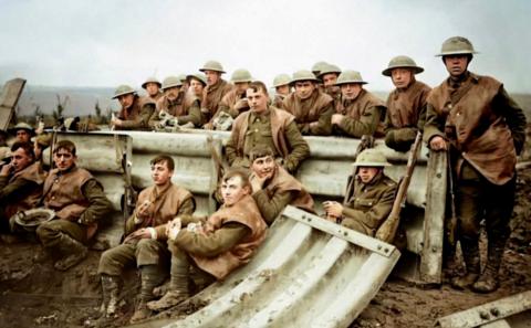The photo, once black and white and now coloured, shows soldiers from the Severn Valley Pioneer regiment posing for the camera next to metal panels used to reinforce trench walls. It is an artistic rendition of original black and white material. They are wearing brown tunic tops, green uniform and army boots. Some are wearing army helmets.
