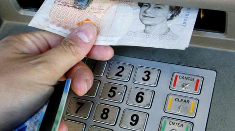A stock image of a hand pulling a £10 note out of a cash machine.