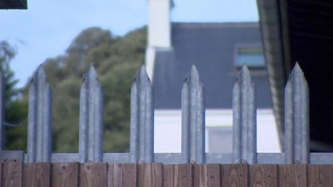 A picture of the outside of Greenfields secure accommodation, including the spokes of metal fence and a white house behind it.