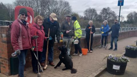 A group of people carrying brooms to help clean up the pavements in the community.