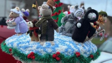 Several colourful knitted characters from the Charles Dickens' novella, 'A Christmas Carol'. The characters are depicted as mice dressed in period costume and sit as a postbox topper.