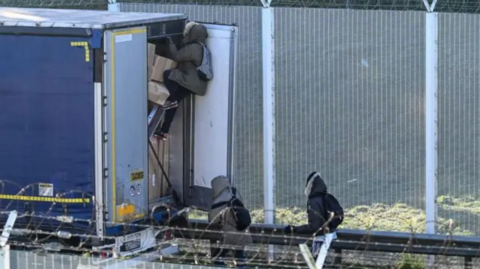 Migrants climbing into the back of a stationary lorry