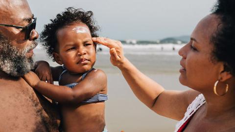 Woman putting sunscreen on small child's face on a beach