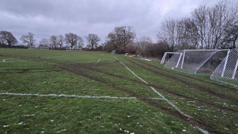A view across football pitches with muddy tyre tracks visible running in several directions