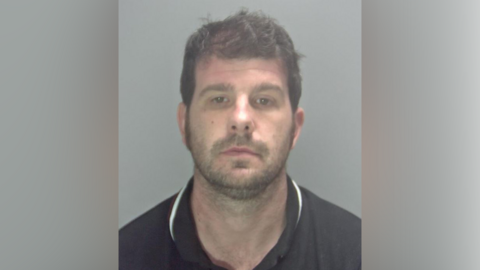 Stuart Worby, pictured in a black or navy-coloured polo shirt, posing for a police custody photo