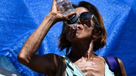A woman drinks water while cooling down in a tent in Phoenix's largest homeless encampment, amid the city's worst heat wave on record on 25 July , 2023
