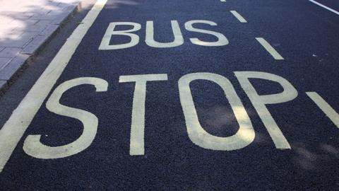 Generic image of a bus stop sign painted in yellow capitals against the black asphalt of a road