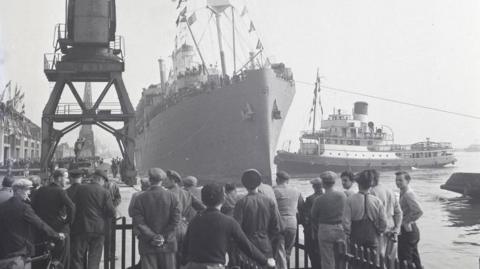 Archive image of a ship coming into docks in Southampton with dock workers looking on