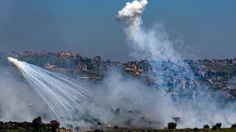 Two explosions of white smoke in front of a hillside - the Lebanese side of the border with Israel