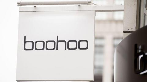 Clos-up of a square, white hanging sign on a shop saying "boohoo" in black text